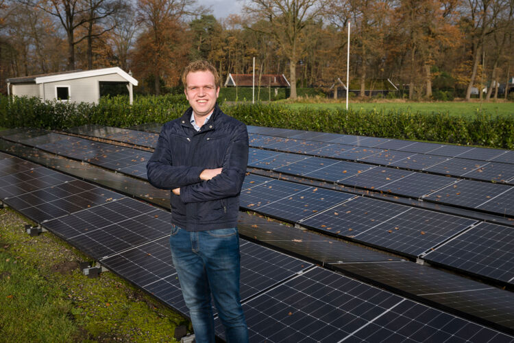 Man in jas staat buiten voor een veld zonnepanelen. 