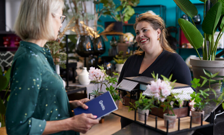 Vrouw in zwart praat met met vrouw in groen met Qredits boekje in bloemenzaak