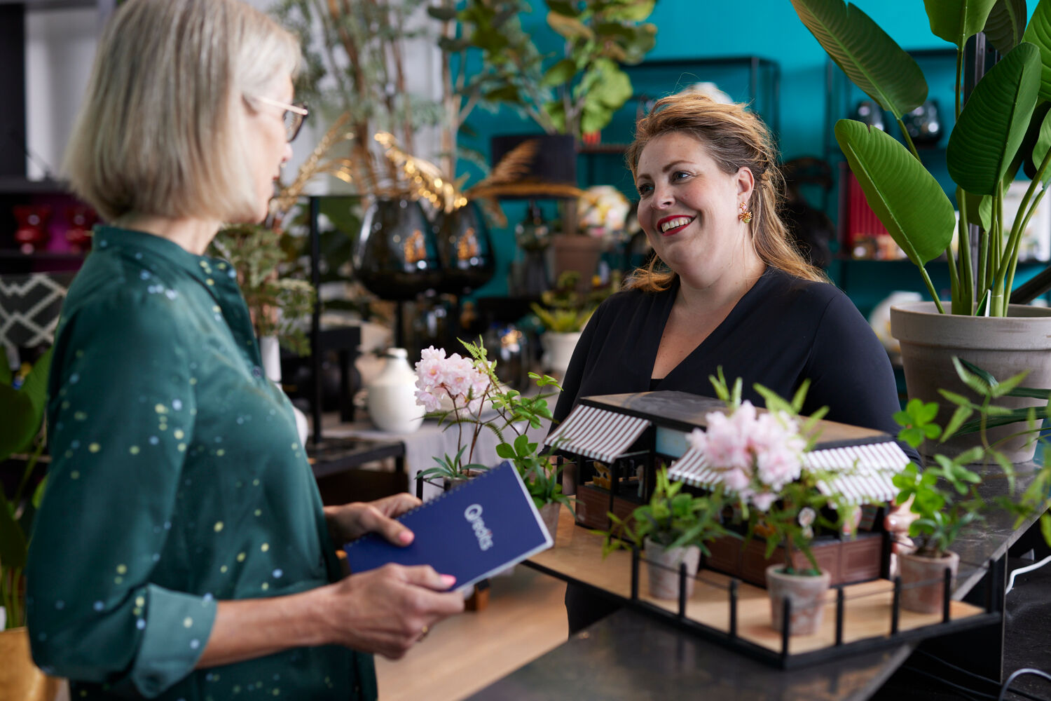 Vrouw in zwart praat met met vrouw in groen met Qredits boekje in bloemenzaak