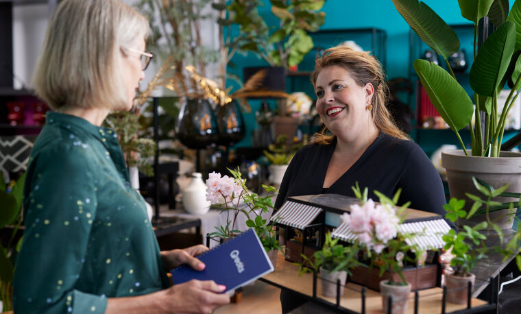 Vrouw in zwart praat met met vrouw in groen met Qredits boekje in bloemenzaak