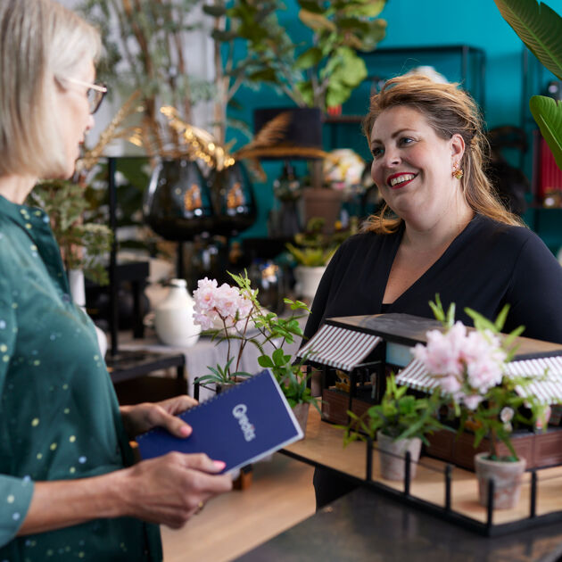 Vrouw in zwart praat met met vrouw in groen met Qredits boekje in bloemenzaak