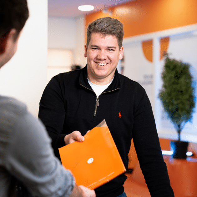 Man in zwart shirt geeft een oranje document aan andere man