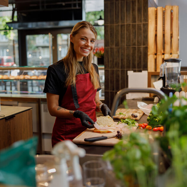 Lachende vrouw met een rood schort is eten aan het bereiden.