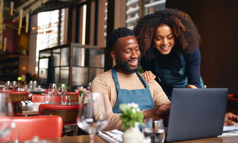 Man en vrouw kijken naar laptop in restaurant.