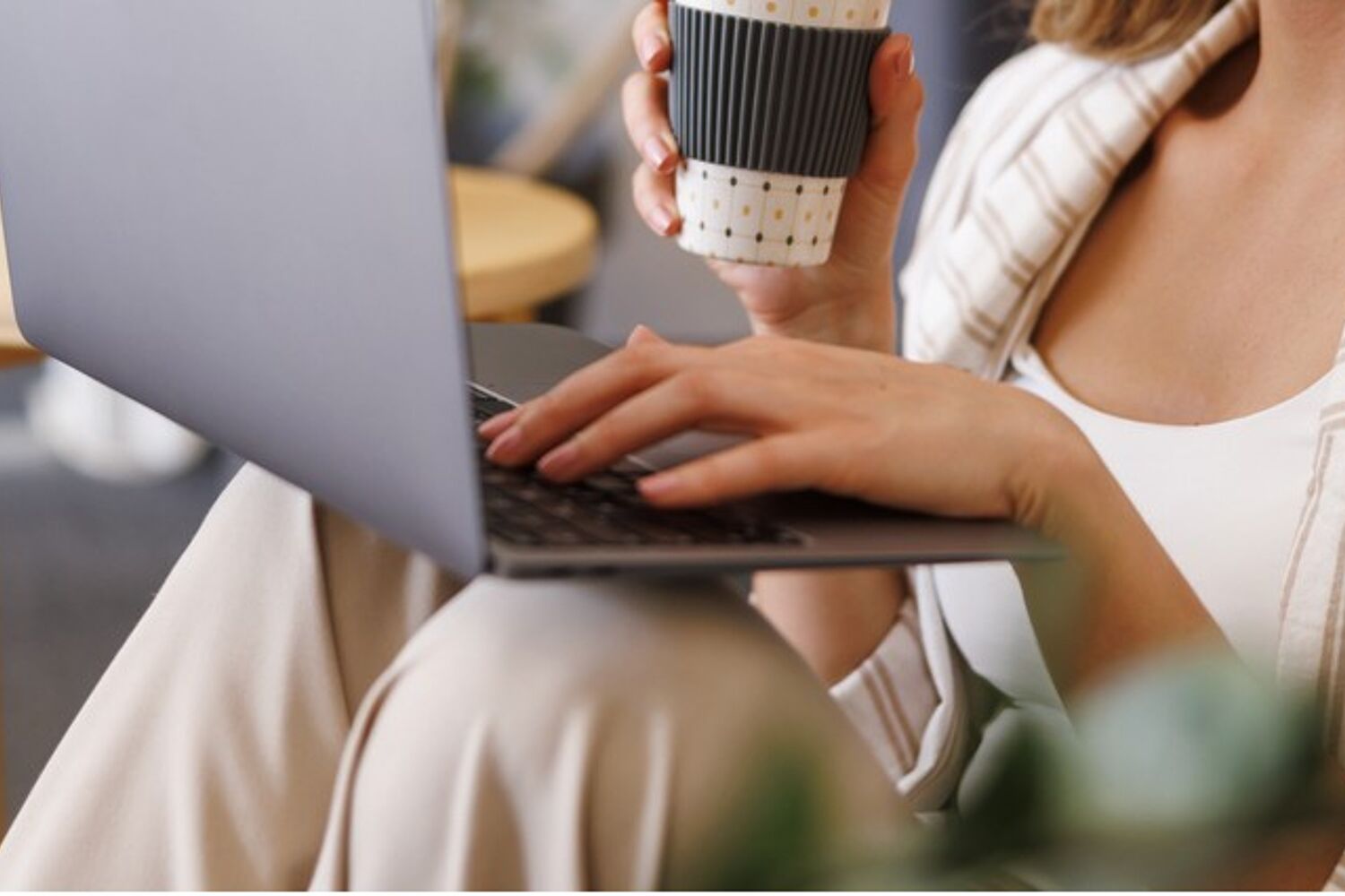 Vrouw met koffiebeker en laptop op schoot, typt op laptop.