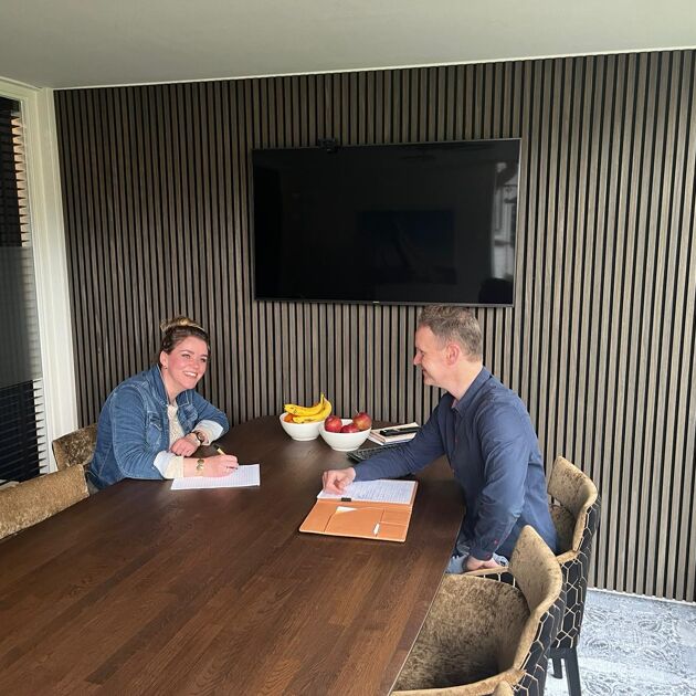 Man in blauw shirt en vrouw in spijker jasje zitten aan tafel en praten