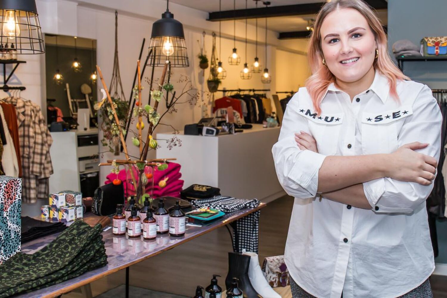 Eigenaresse van winkel staat met armen over elkaar lachend in de winkel