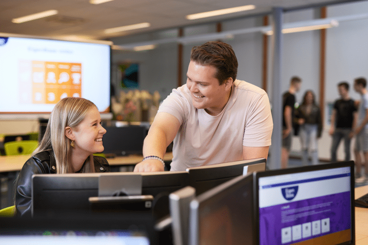 Man in roze shirt helpt leerling bij computer