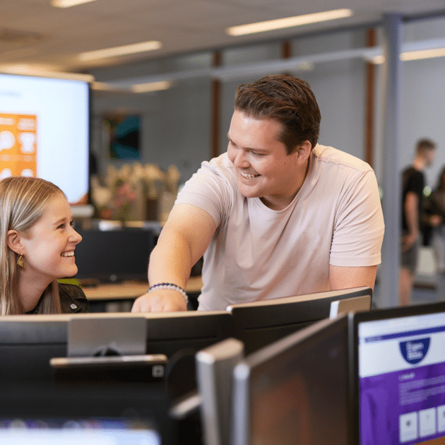 Man in roze shirt helpt leerling bij computer