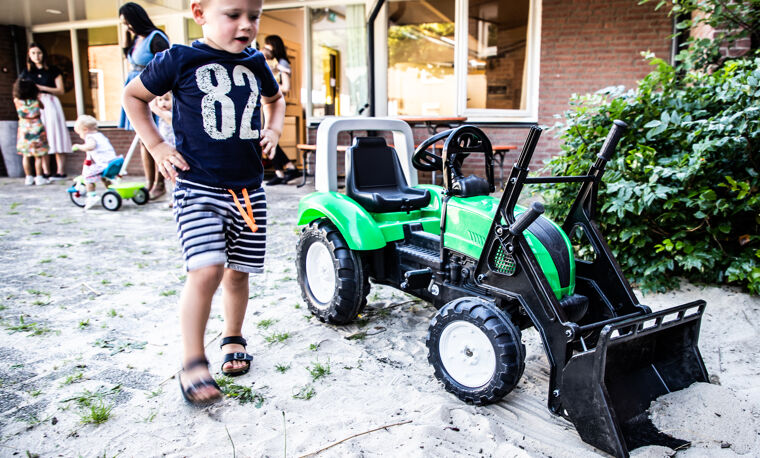 Kleine jongen loopt naar zijn speelgoed tractor toe en kijkt ernaar