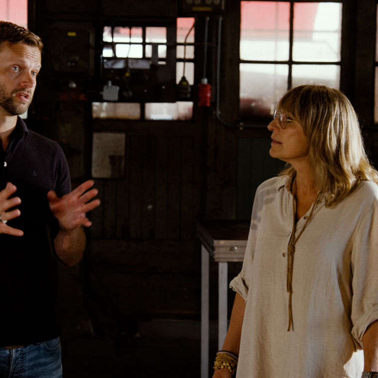 Man in zwart shirt spreekt tegen vrouw in wit shirt in donkere ruimte