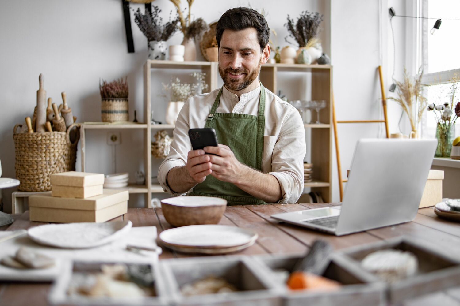 Man met schort aan zit en kijkt naar zijn mobiel. 