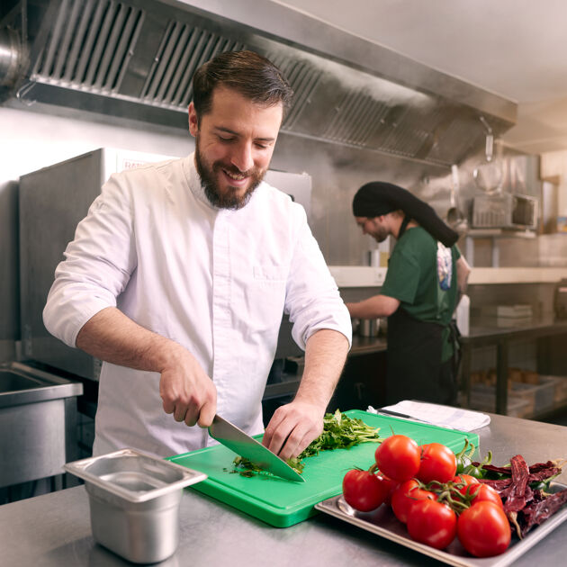 Man staat in de keuken en snijdt groente.