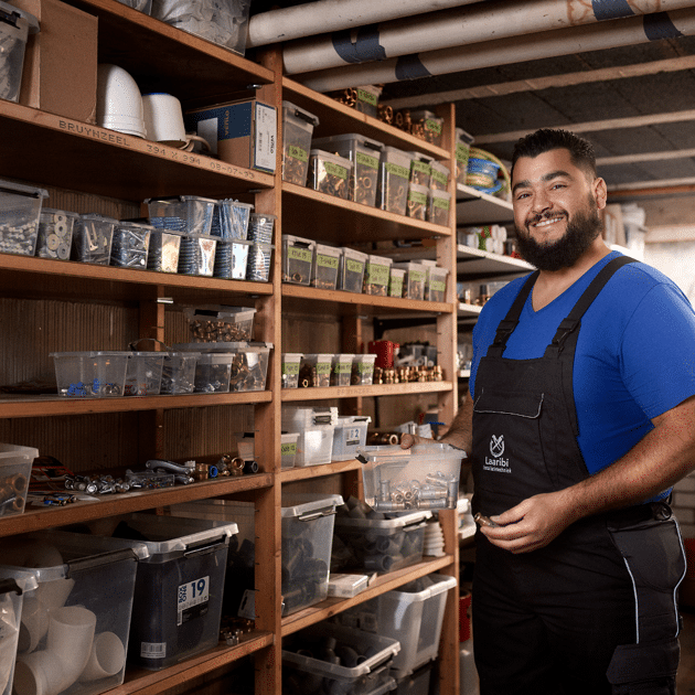 Man staat in een schuur met een bakje met gereedschap in zijn hand