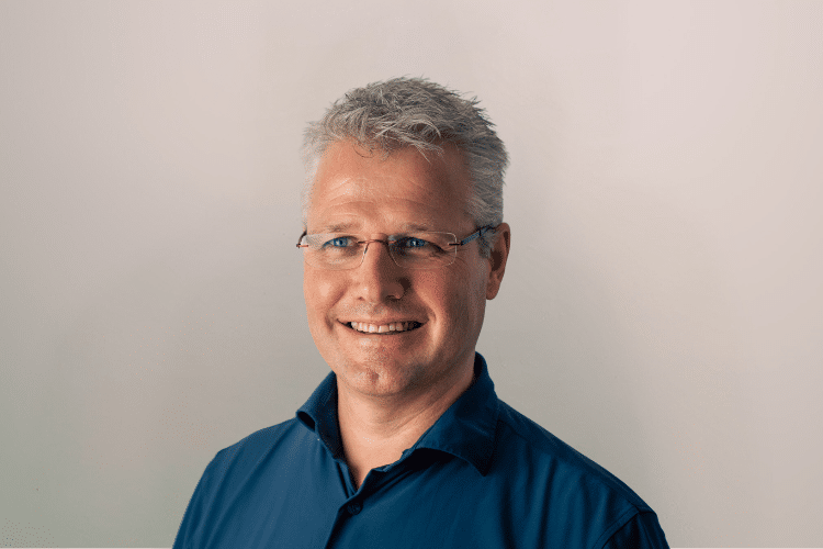 Chris medewerker Qredits man in blauw shirt voor grijze achtergrond