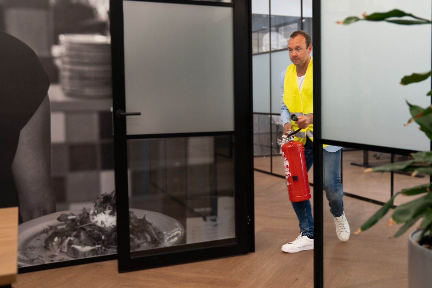 Man met geel hesje en brandblusser rent naar binnen. 