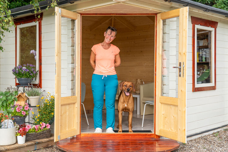 een vrouw met roze shirt staat in een tuinhuisje met haar hond