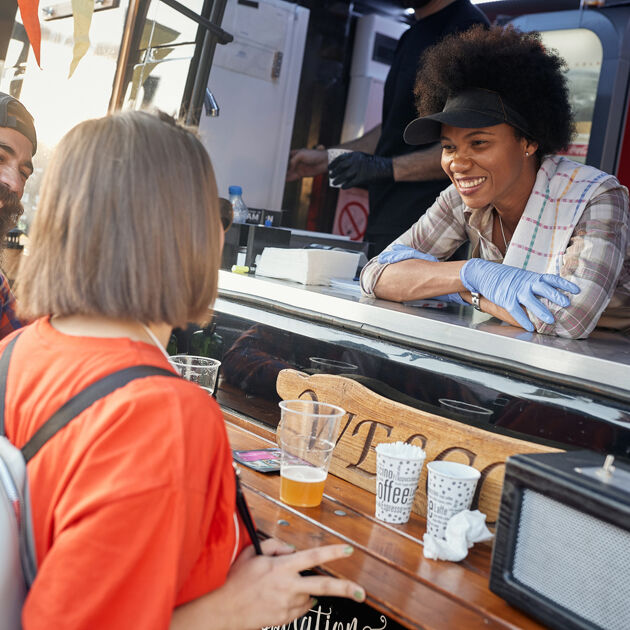 Vrouw staat in foodtruck en kijkt lachend naar klanten.
