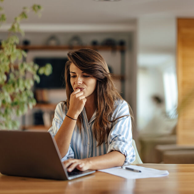 Vrouw met bruin haar kijkt bedenkelijk naar laptop.
