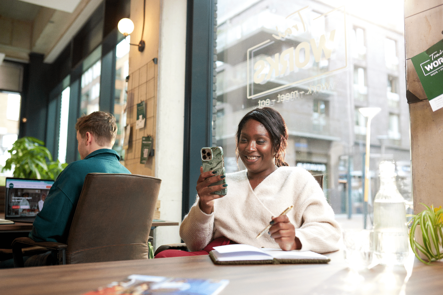 Vrouw kijkt op haar telefoon en schrijft in een schrift