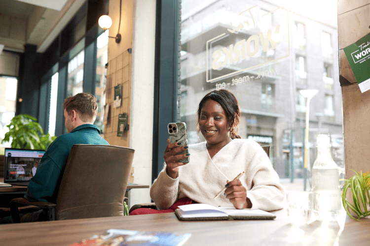 Vrouw kijkt op haar telefoon en schrijft in een schrift
