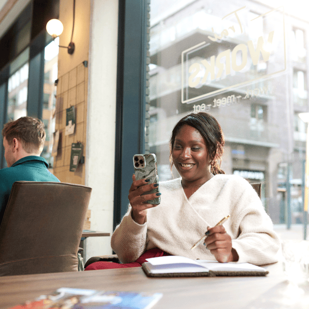 Vrouw kijkt op haar telefoon en schrijft in een schrift