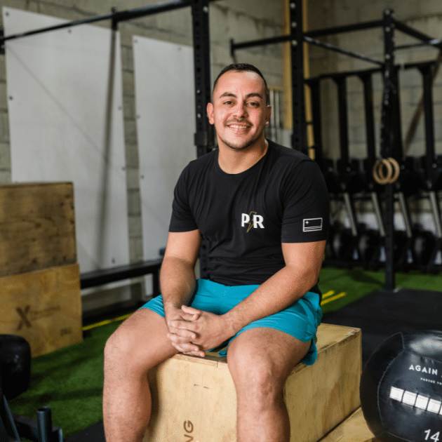 Man in zwart shirt en blauwe broek zit op doos in sportschool