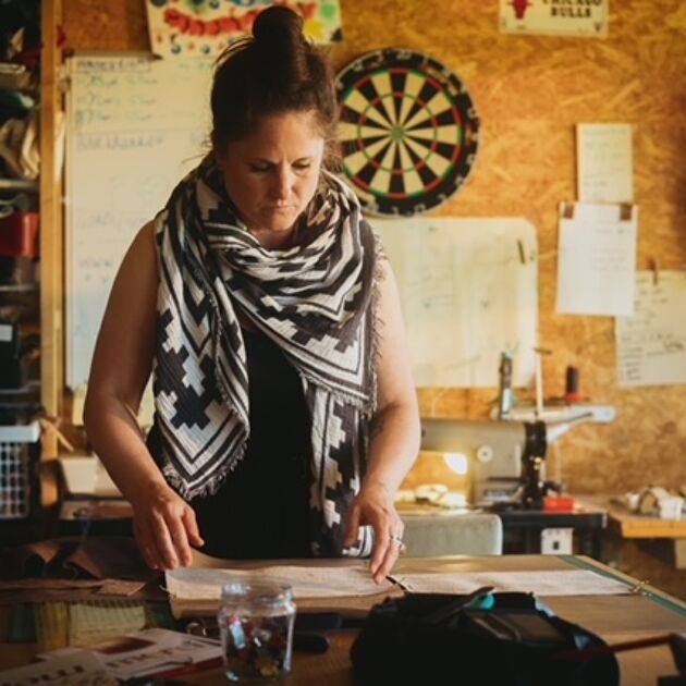 Vrouw met een sjaal om staat achter een werkbank en kijkt naar papieren.