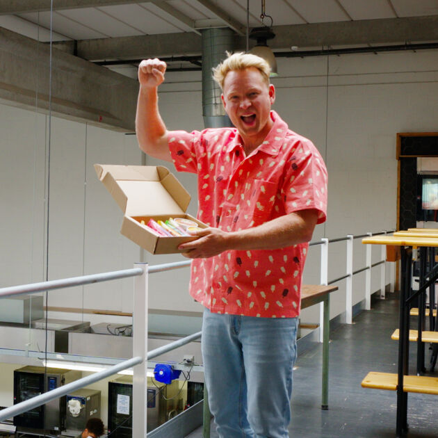 Blije man in roze shirt houd een doos ijsjes ast en heeft zijn vuist in de lucht