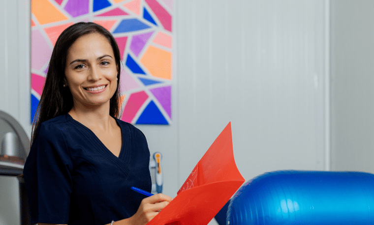 Vrouw in blauwe bloes schrijft in een mapje in een fysiotherapie praktijk