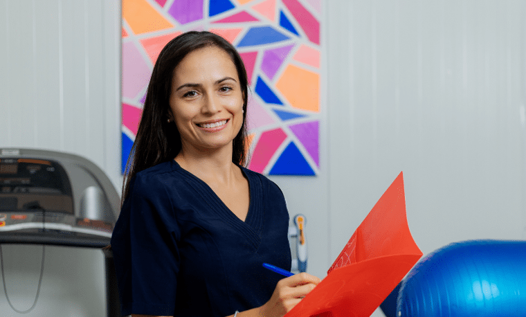 Vrouw in blauwe bloes schrijft in een mapje in een fysiotherapie praktijk