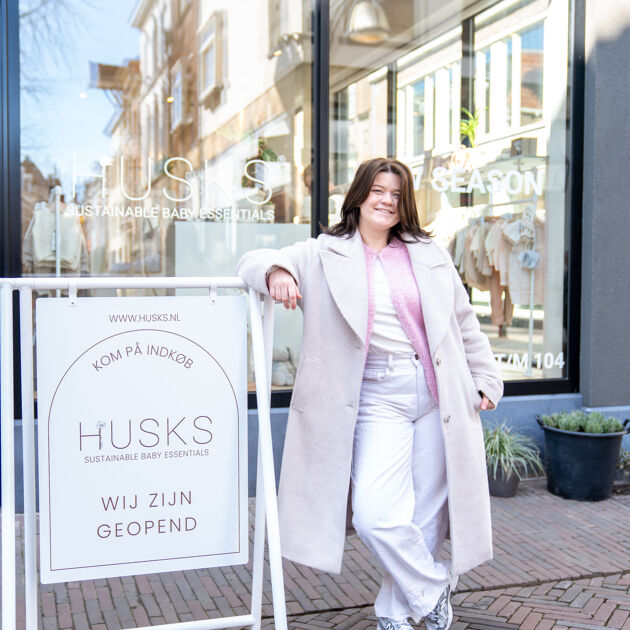 Vrouw staat trots voor haar winkel bij het reclamebord.