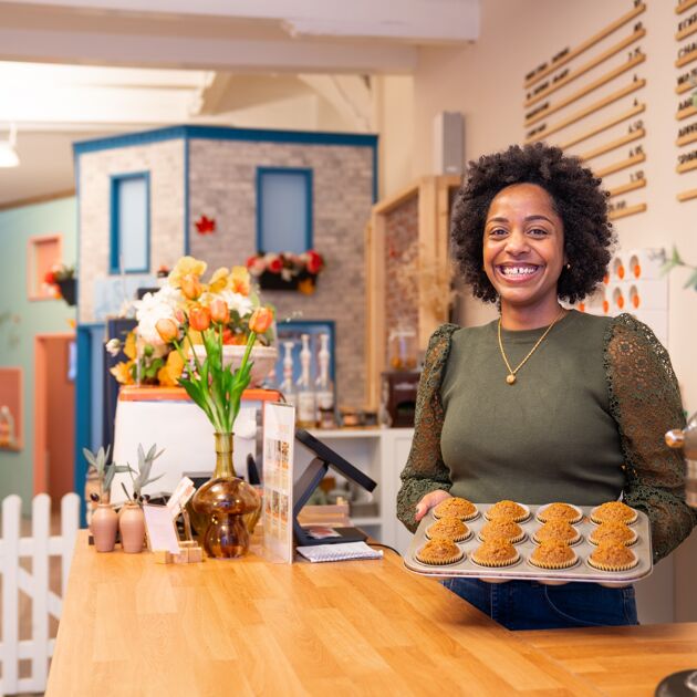 Een lachende vrouw staat met cupcakes achter een balie. 