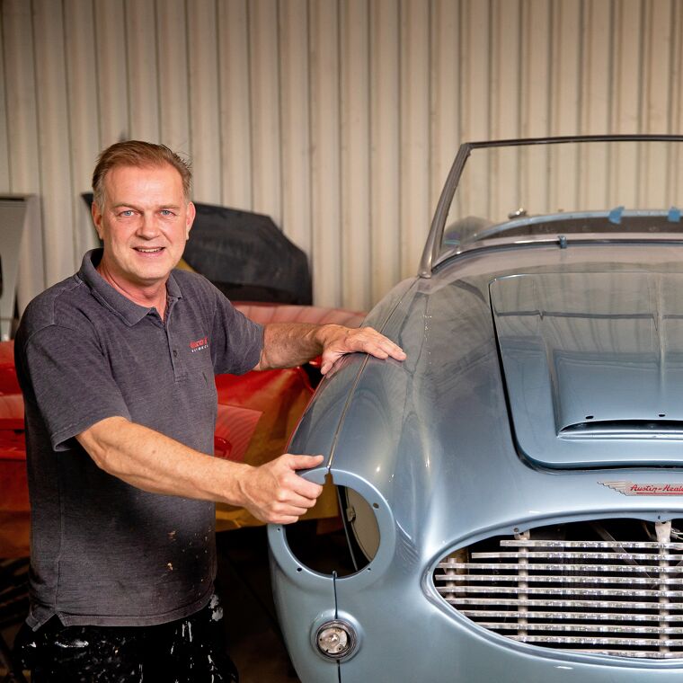 Man in grijs shirt werkt aan een oude grijze auto