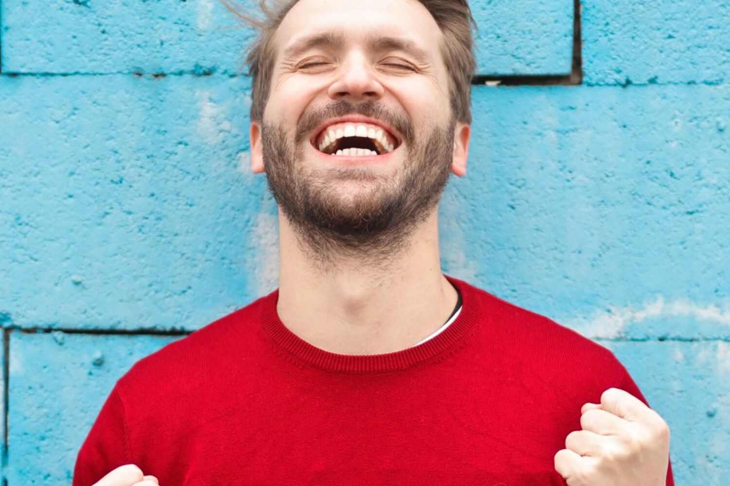 Man met een rood shirt heeft zijn ogen dicht en juicht 