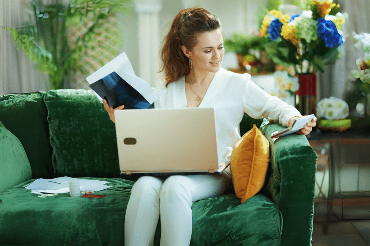 Vrouw zit op de bank met een laptop, schrift en rekenmachine.