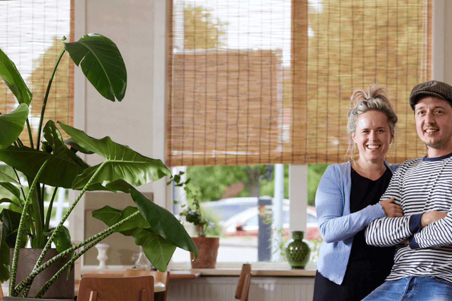 Man en vrouw staan in kamer met grote plant veel tafels en stoelen