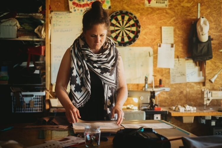Vrouw met een sjaal om staat achter een werkbank en kijkt naar papieren.