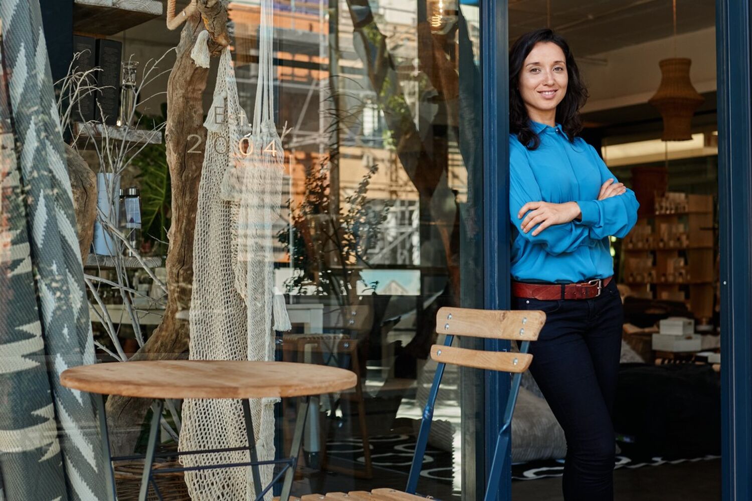 Vrouw met blauwe blouse aan en handen over elkaar leunt tegen de deur.