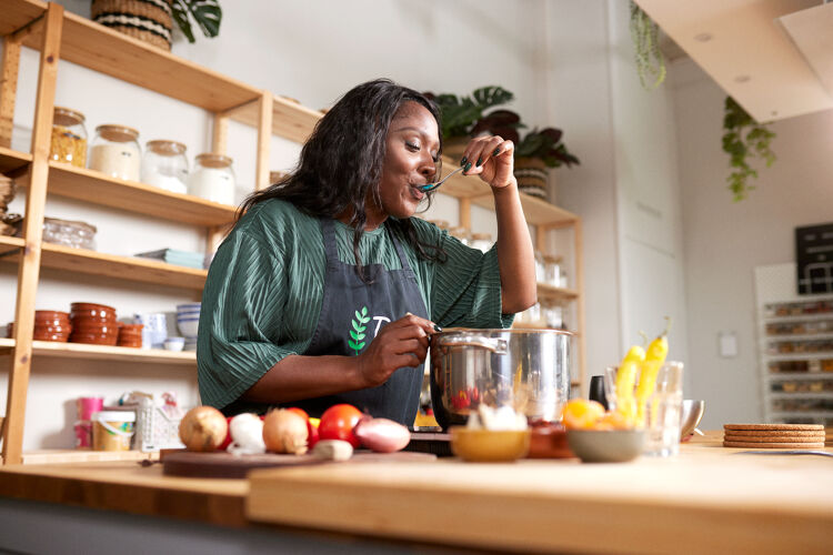 Vrouw met groen shirt staat in de keuken en proeft soep.