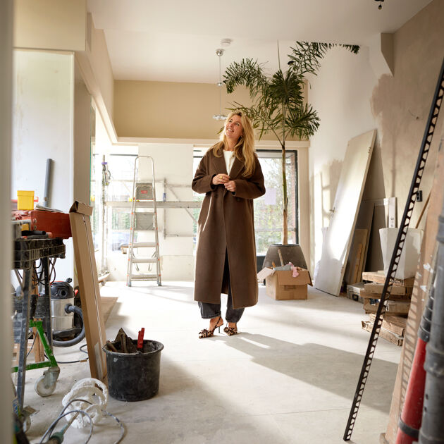 Vrouw staat op bouwplaats en kijkt dromend weg.