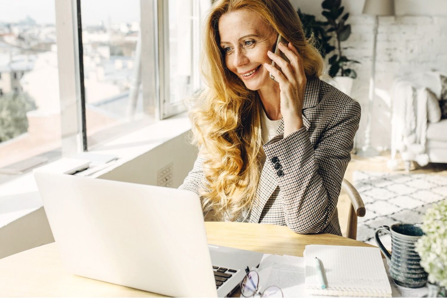 Vrouw kijkt lachend naar haar laptop terwijl ze aan het bellen is. 