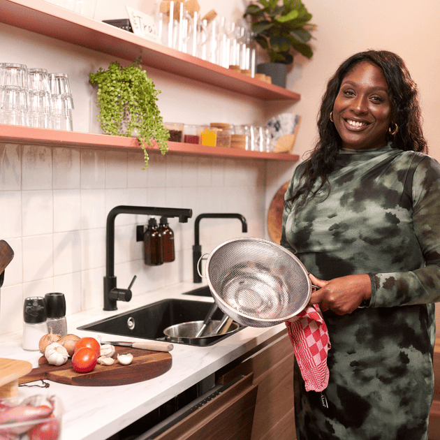 Vrouw staat in een keuken met een theedoek en zeef in haar handen
