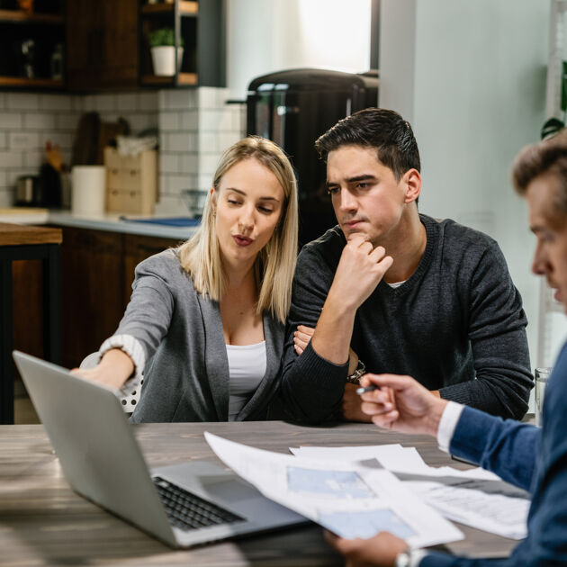 Vrouw wijst naar laptop en praat, twee mannen kijken naar laptop. 