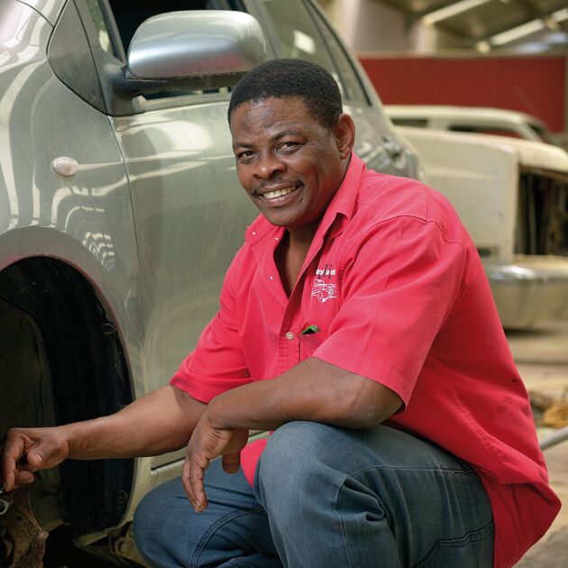 Lachende man in rood shirt hurk naast zilveren auto