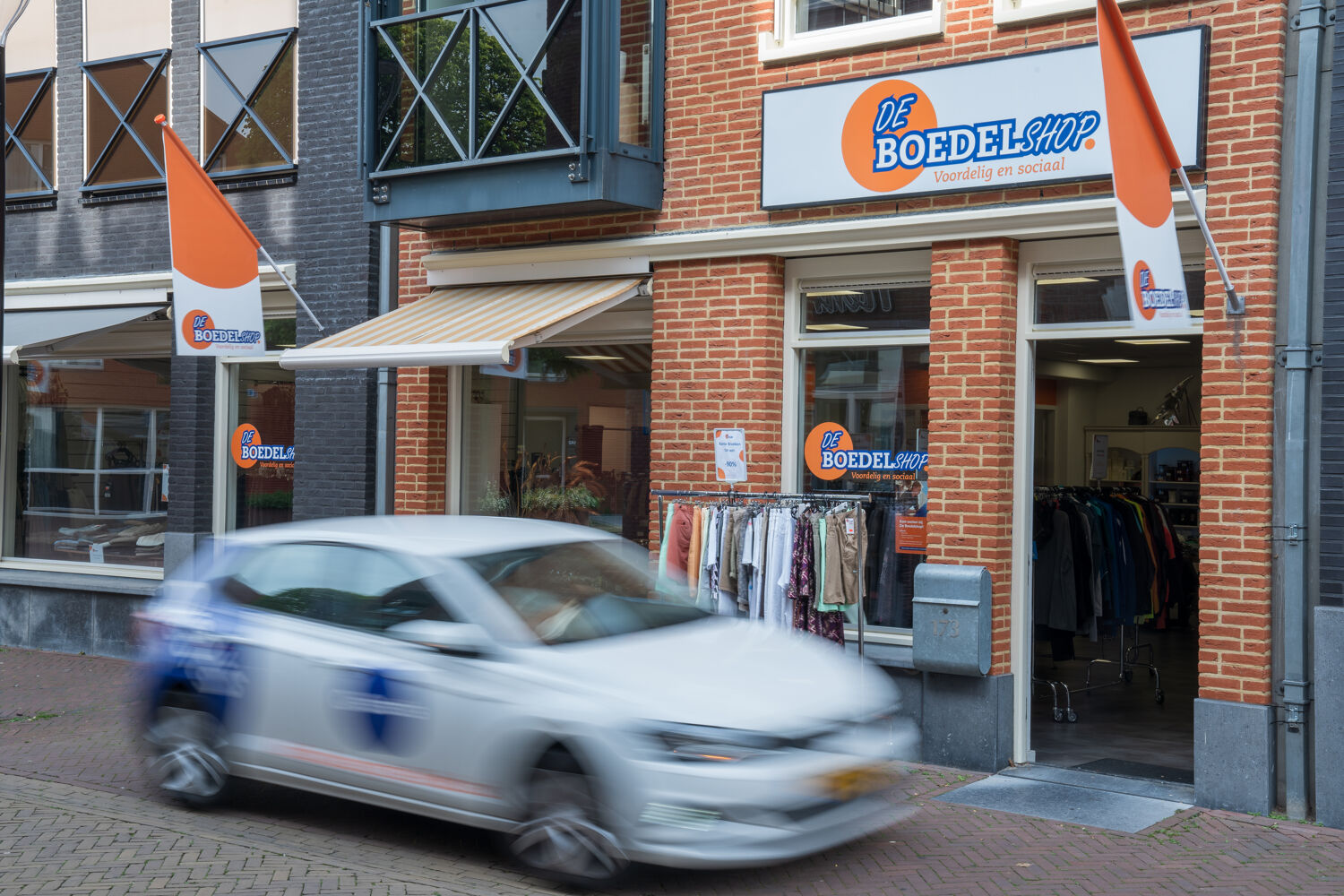 Witte auto rijdt voor de boedelshop met kleding buiten