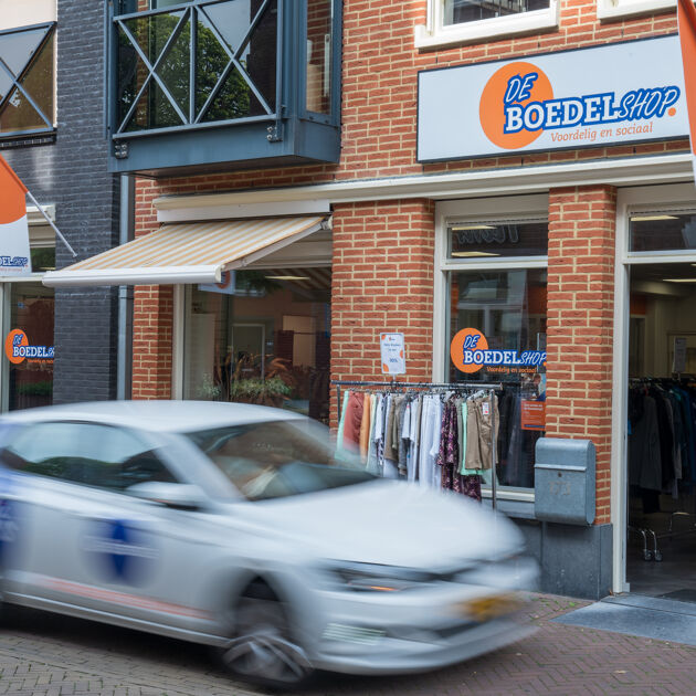 Witte auto rijdt voor de boedelshop met kleding buiten
