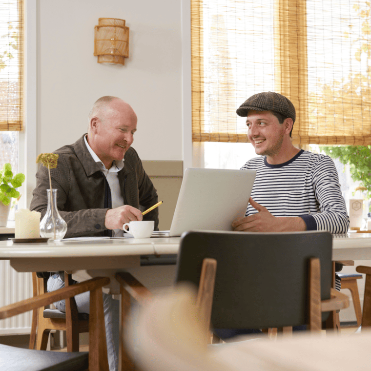 Twee mannen zitten aan een huistafel met laptop en praten