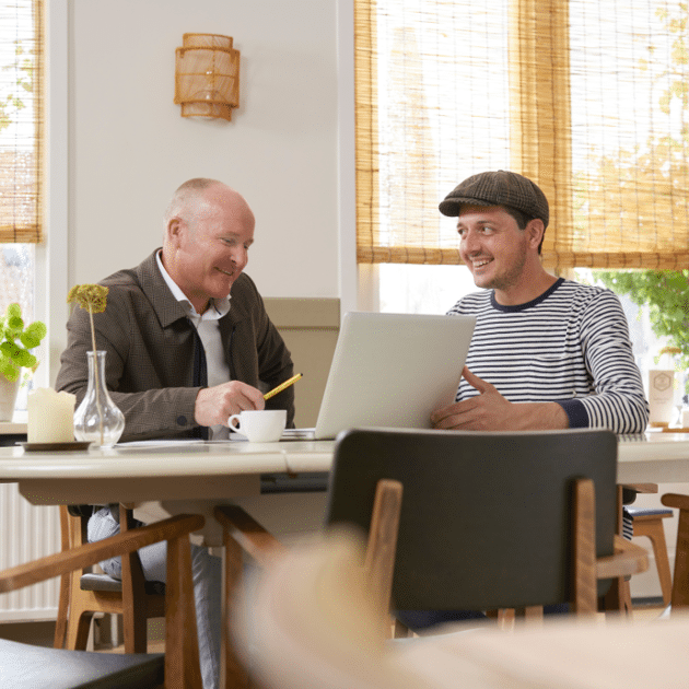 Twee mannen zitten aan een huistafel met laptop en praten