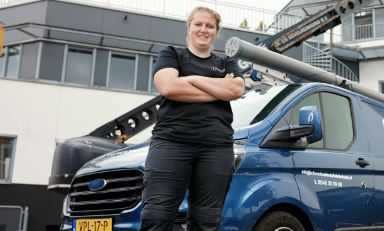 Vrouw in zwarte kleding staat voor een blauwe werkbus